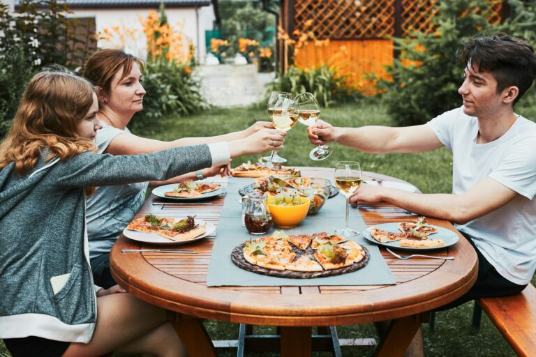 Friends making toast during summer picnic outdoor dinner in a home garden. Weekend family dinner